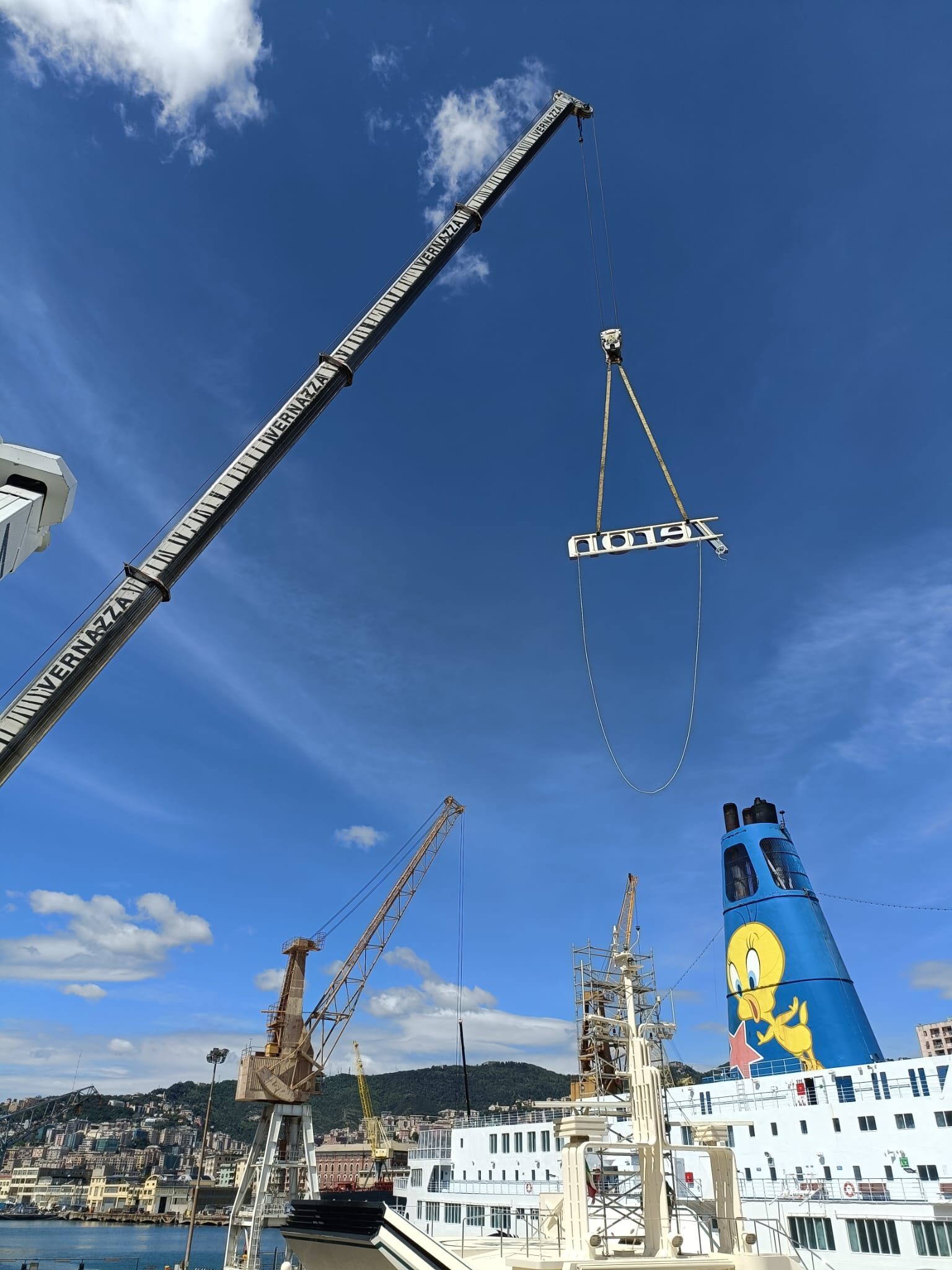 Crane lifting the illuminated Accelleron sign at a shipyard, with a passenger ferry in the background