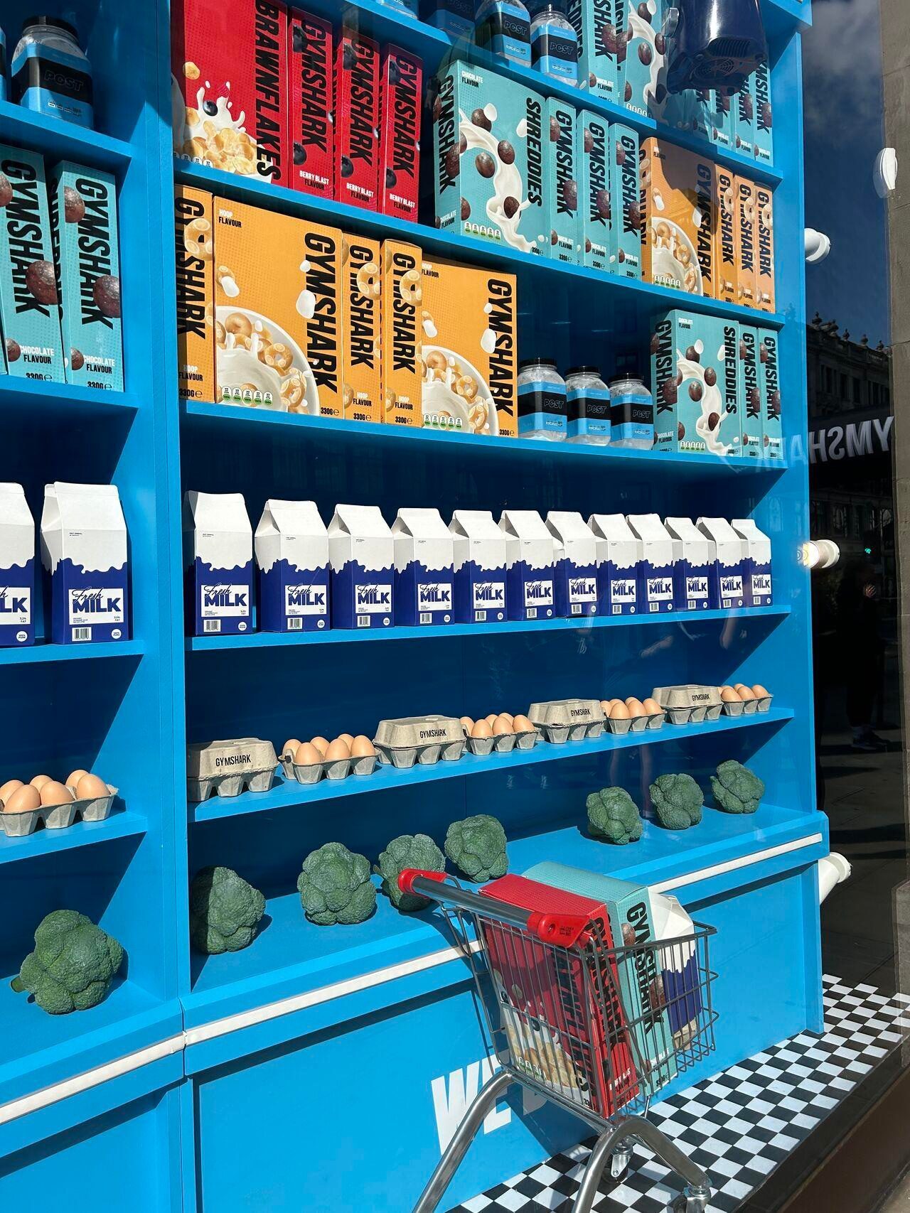 Close-up of Gymshark-branded grocery display props: cereal boxes, milk cartons, eggs and broccoli