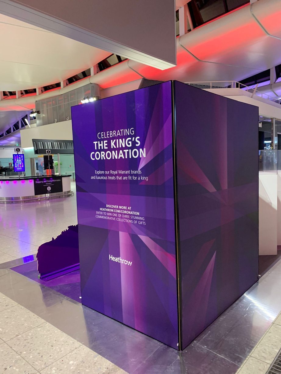Illuminated purple King's Coronation column wrap display in a Heathrow terminal at night