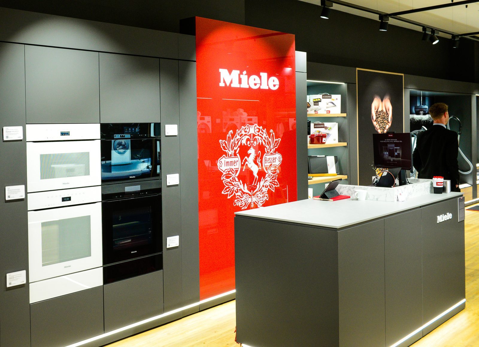 Miele in-store counter area with red branded panel and 'Immer Besser' crest signage